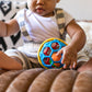 Baby holding a blue and green ball rattle with yellow rim and colored segments