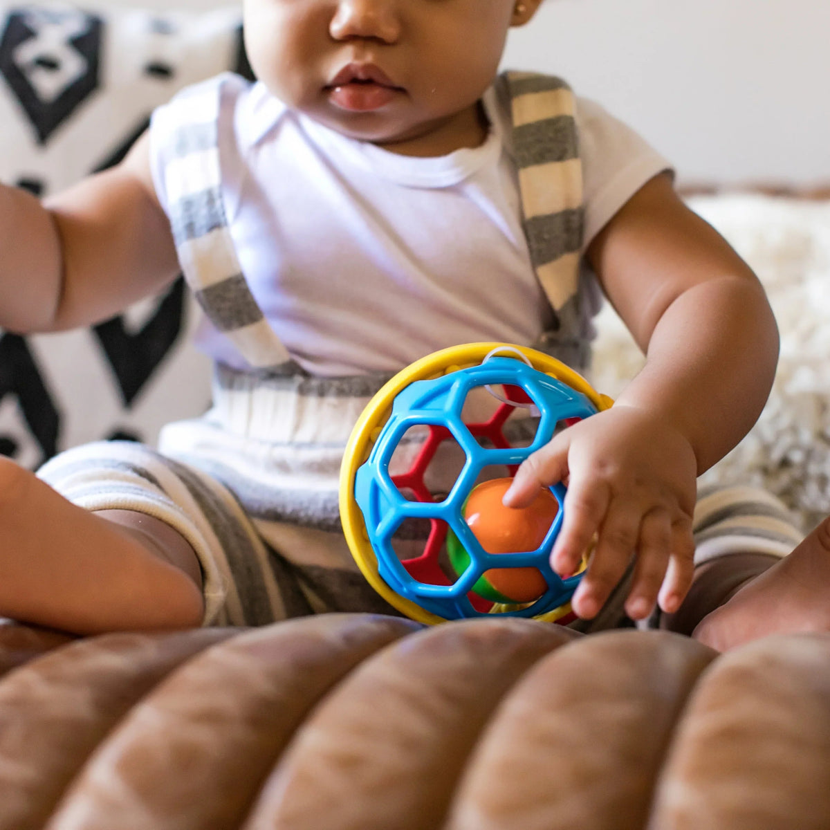 Baby holding a blue and green ball rattle with yellow rim and colored segments