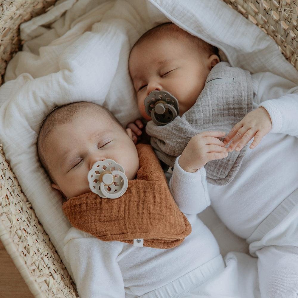 Baby holding two neutral pacifiers with round floral shields and clip-on handles