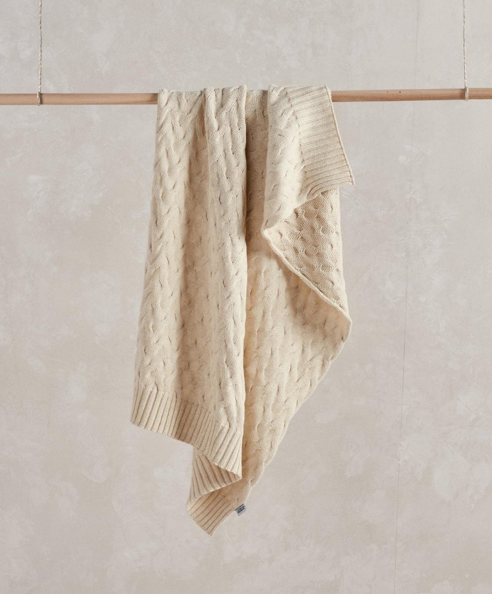 Cream cable-knit baby blanket with cable pattern and fringed edges
