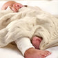 Cream cable-knit baby blanket draped over a newborn, showing cable texture