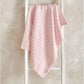 Pink striped chenille blanket with textured knit pattern, draped over a stand