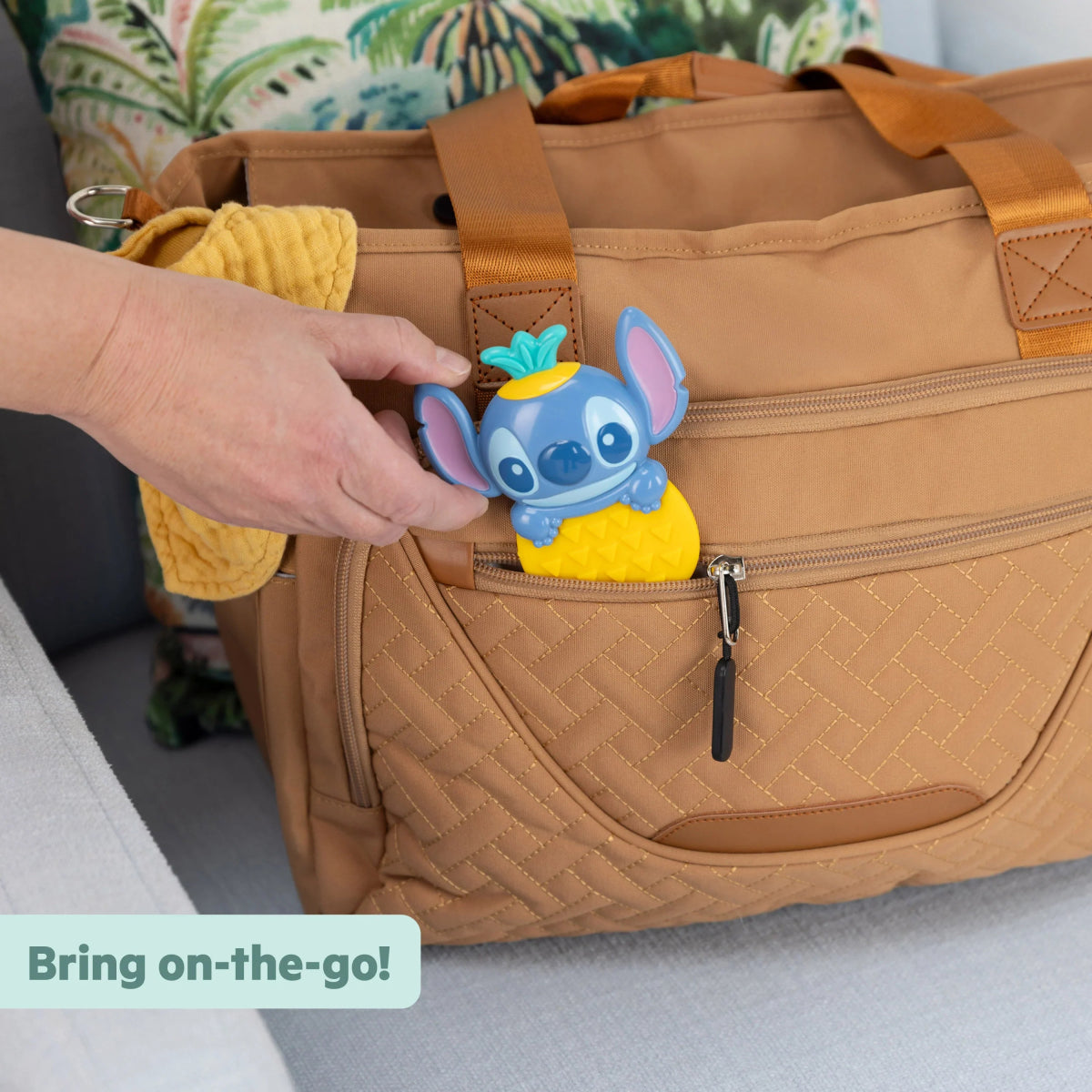 Stitch tropical teether rattle clipped in a tan diaper bag pocket