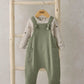 Green dungarees with adjustable bow straps over speckled long-sleeve bodysuit