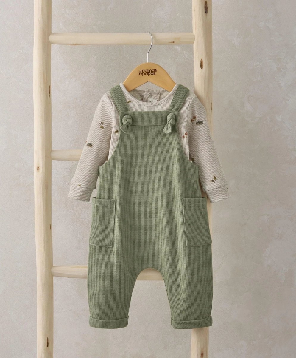 Green dungarees with adjustable bow straps over speckled long-sleeve bodysuit