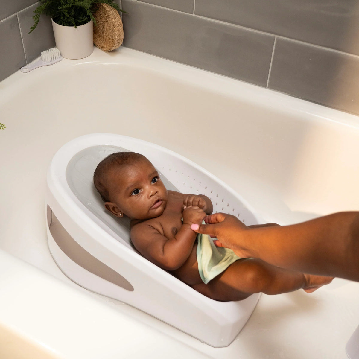 Baby in white bather tub with gray insert and water drain holes