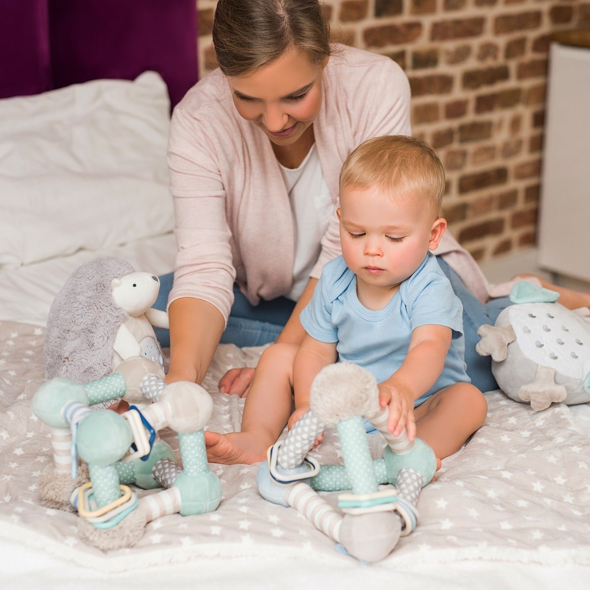 Plush activity pyramid toy on play mat with mint, blue, and striped hanging pieces
