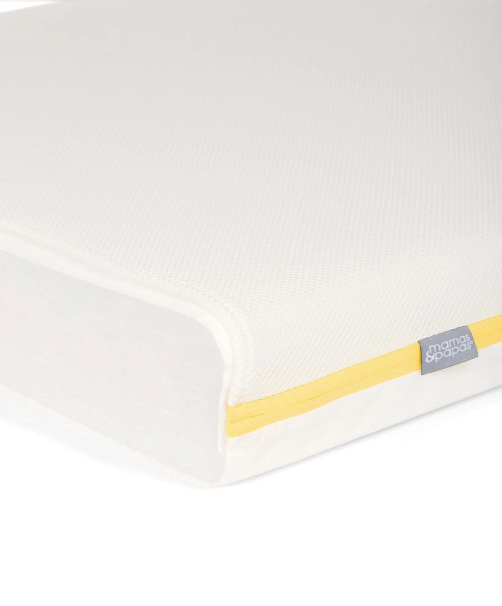 Cotbed mattress corner close-up, white cover with yellow piping