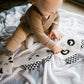 Flat cuddly panda toy on a play mat, with patterned ears and cartoon eyes under a child’s hands