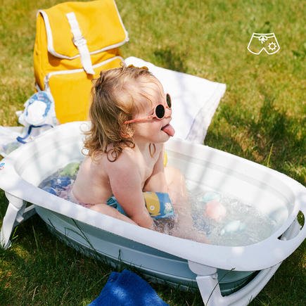 Foldable baby bathtub outdoors with a baby reclining in the light blue bath basin