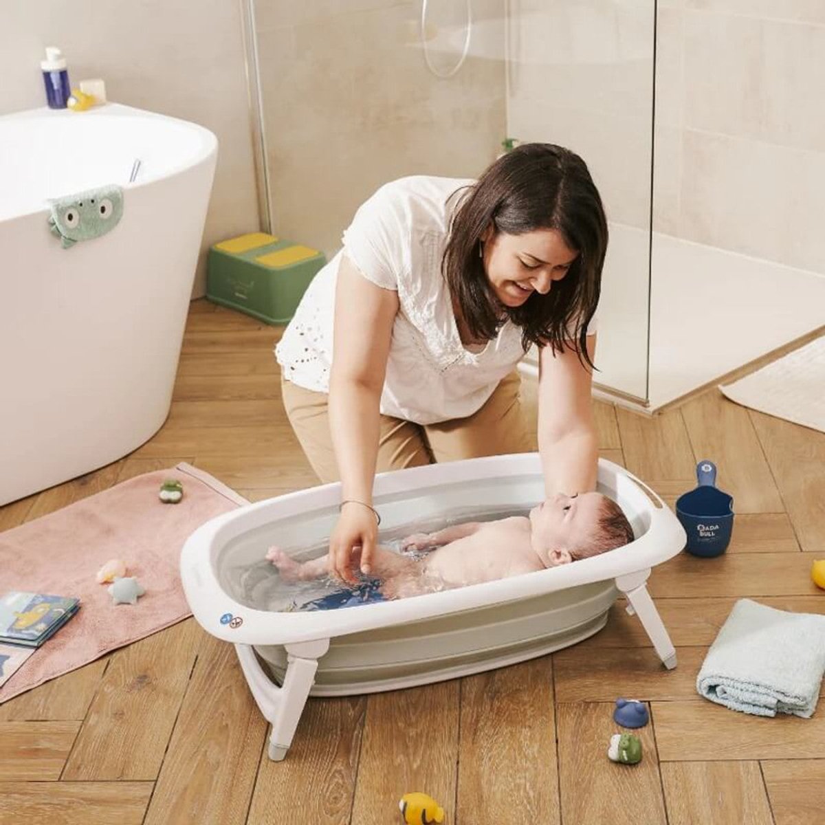 Foldable baby bathtub in a bathroom with a baby being washed, white rim and light blue tub