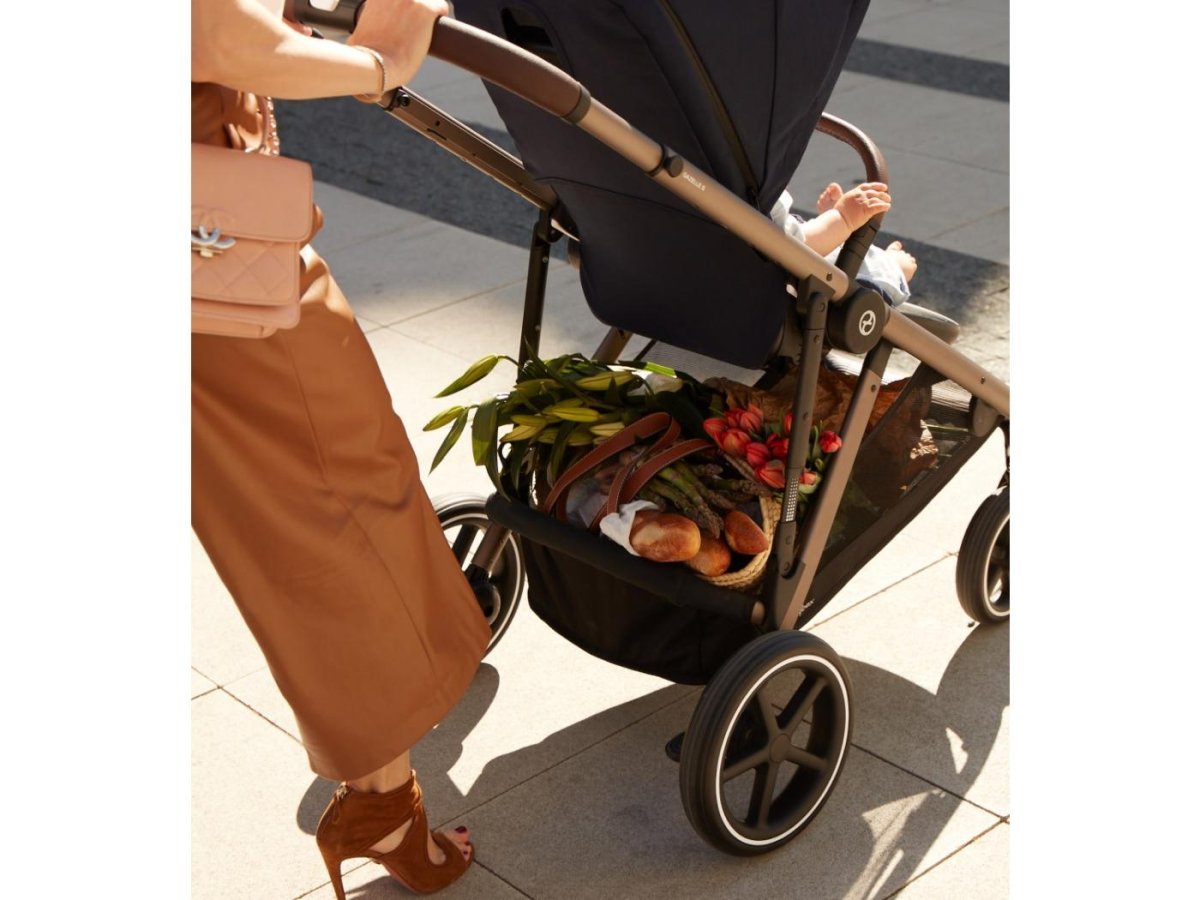 Black stroller with handlebar and front basket holding stored items, side view