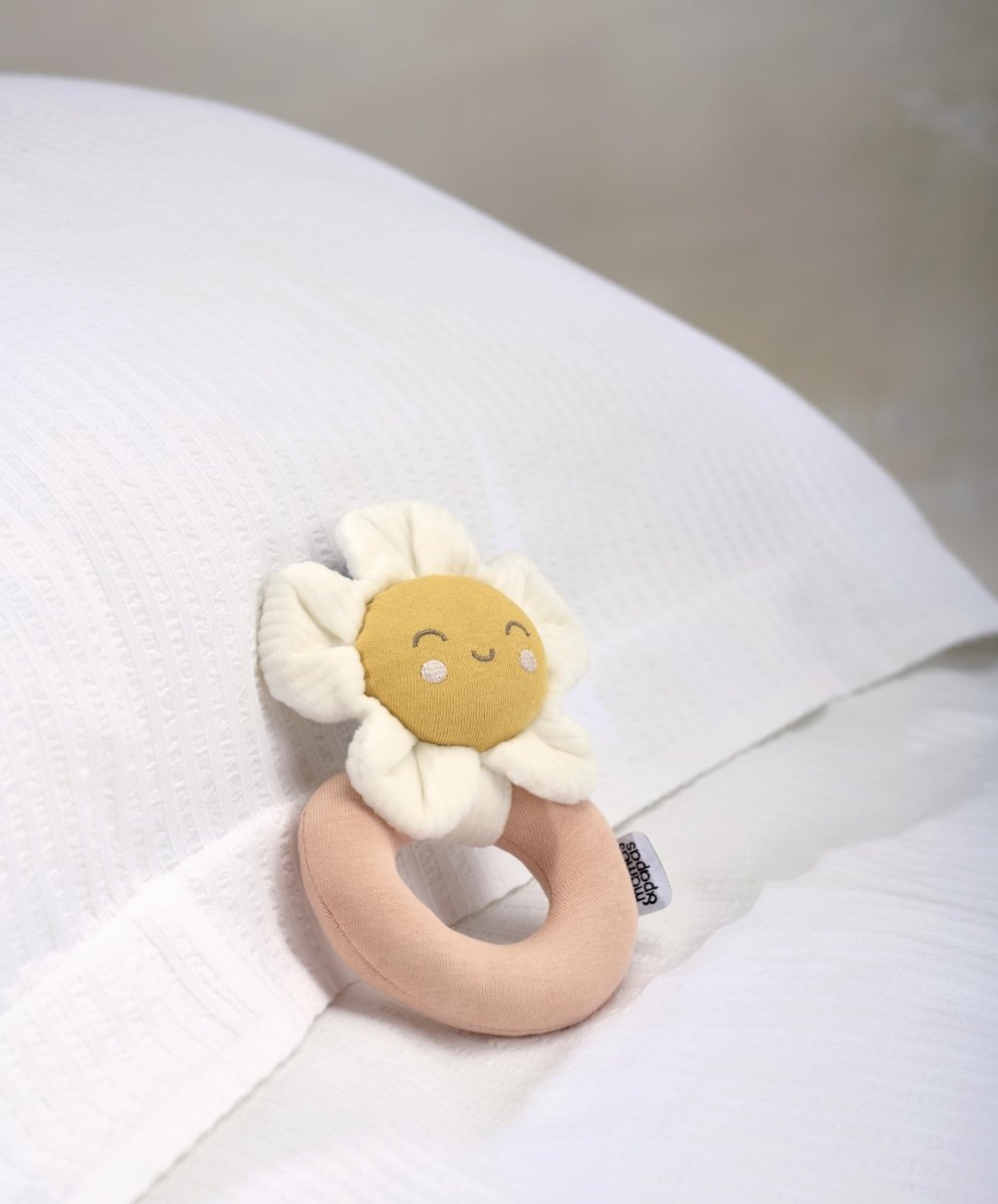 Flower grabber ring rattle toy with white petals, tan ring, yellow smiling face