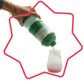 Green milk dispenser tilted by hand, pouring into a small bottle with red-ring base