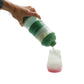 Green milk dispenser held above bottle, dispensing into a small bottle with seal cap