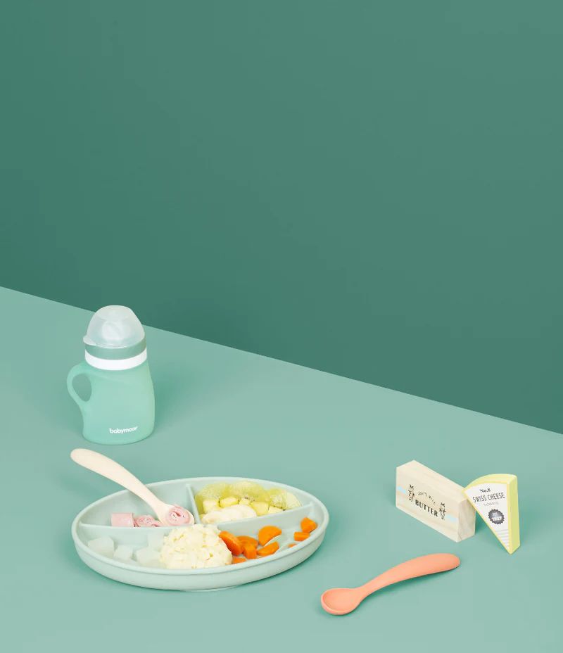 Silicone feeding bowl with spoon and mint baby bottle on table