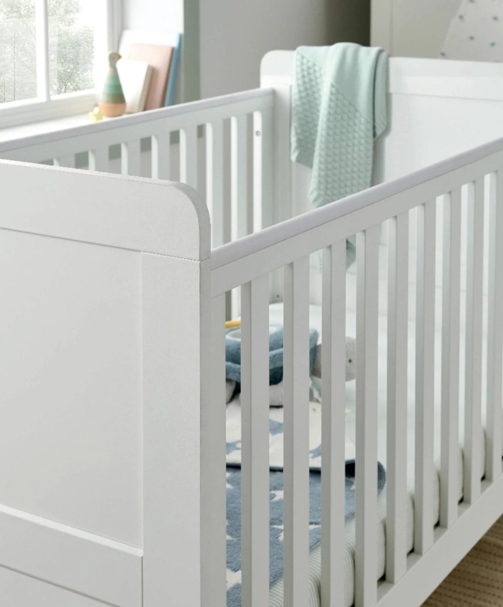 White cotbed with slatted rails and mattress, end panel and posts visible