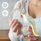 Manual breast pump held with white flange and clear bottle by hands