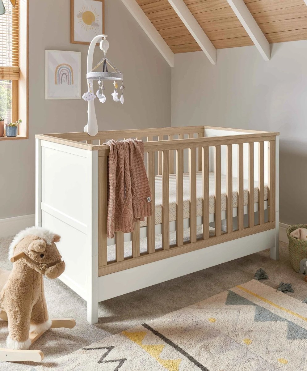 White baby cot with vertical wood slats and a lower drawer cabinet base