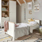 White baby cot with light wood slats and mattress, viewed in a nursery