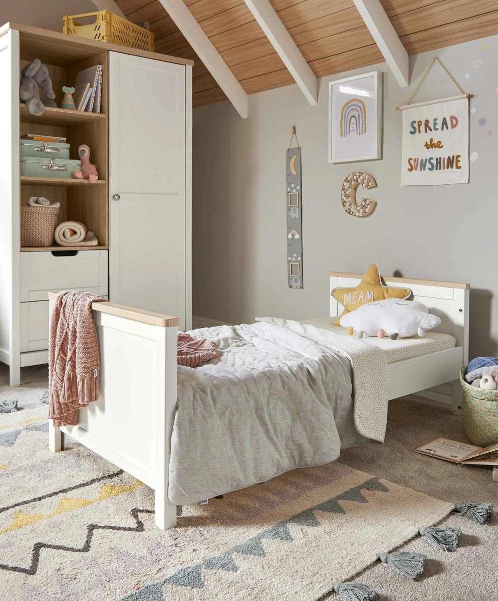 White baby cot with light wood slats and mattress, viewed in a nursery