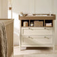 Baby dresser changer beside crib with open shelves and two white drawers, wood top