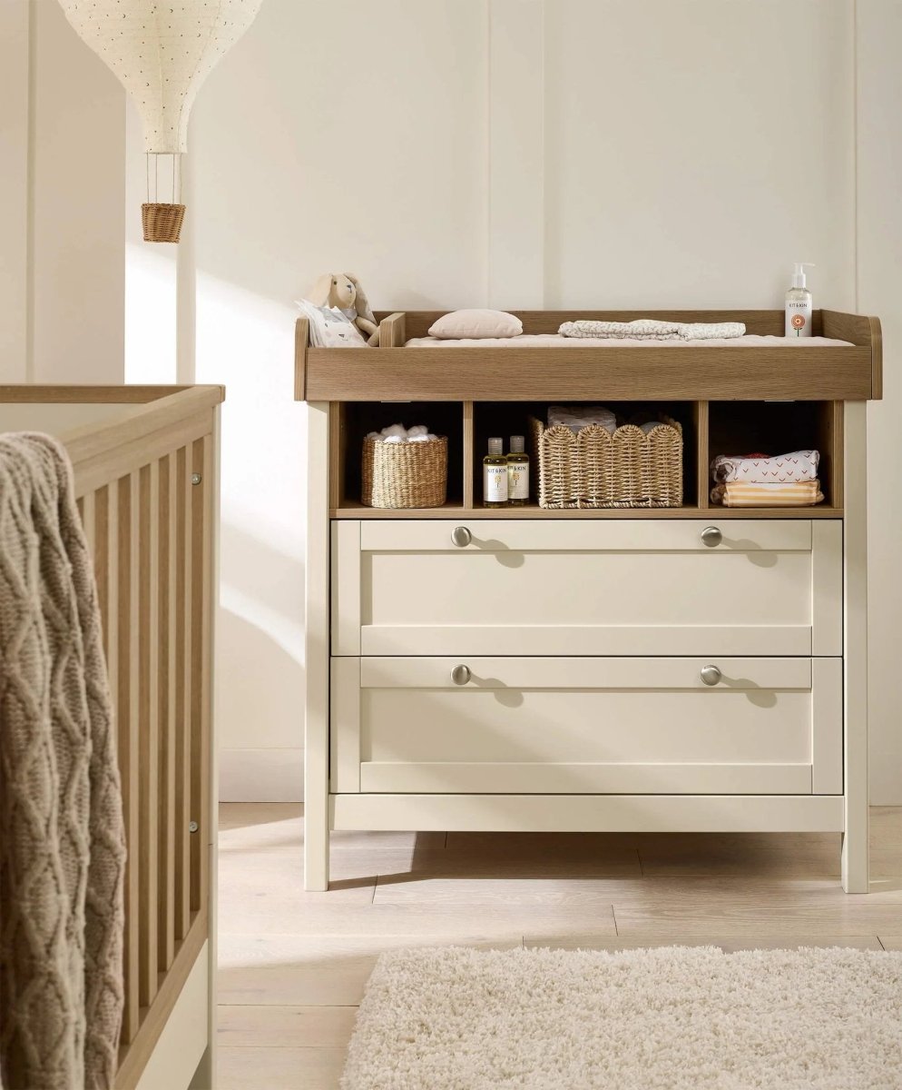 Baby dresser changer beside crib with open shelves and two white drawers, wood top