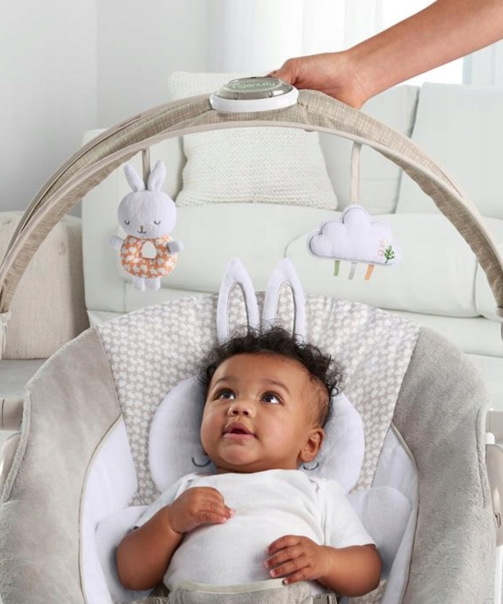 Infant bouncer with grey seat, bunny and cloud plush toys, white headrest