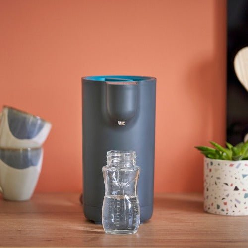 Compact baby bottle warmer with clear bottle in front, dark gray body and teal top.