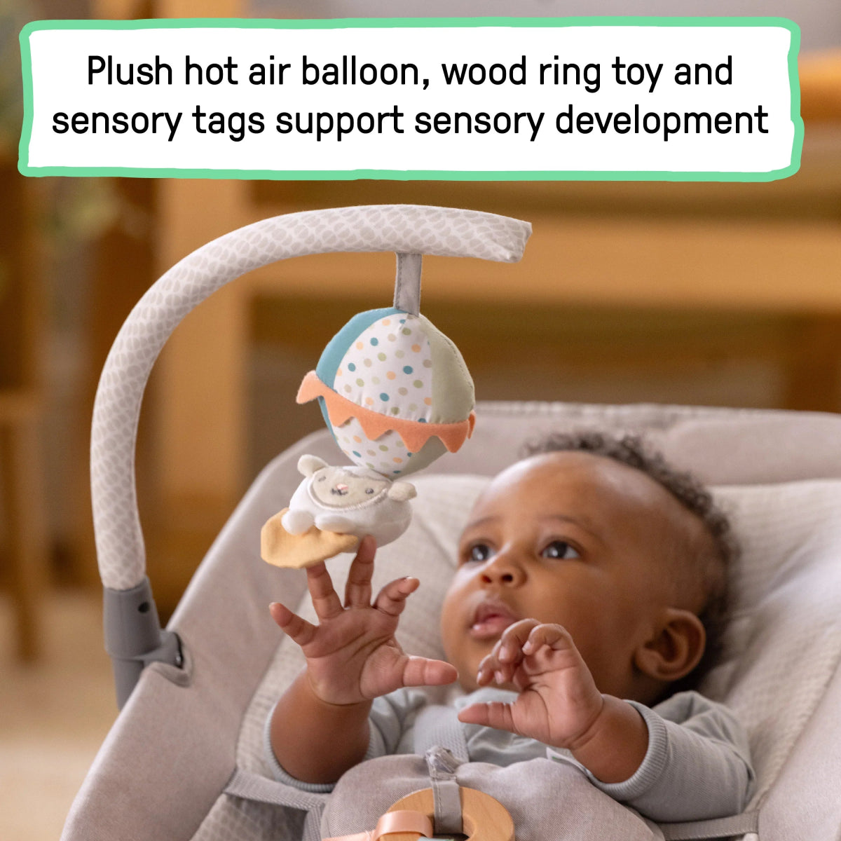 Baby in grey rocking seat with plush mobile toy and dangling fabric tags