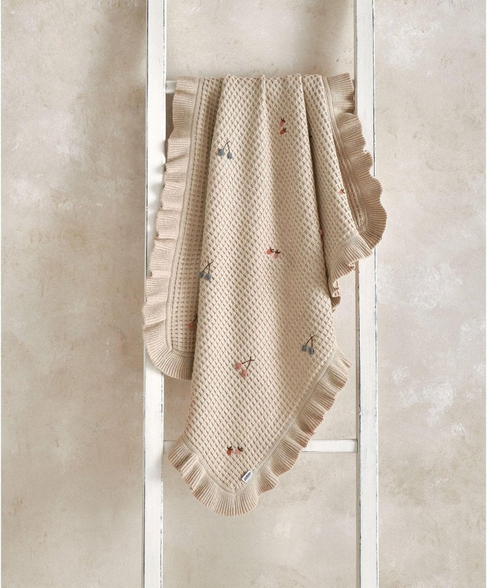 Cream knitted blanket folded with ruffled border and small multicolor motifs