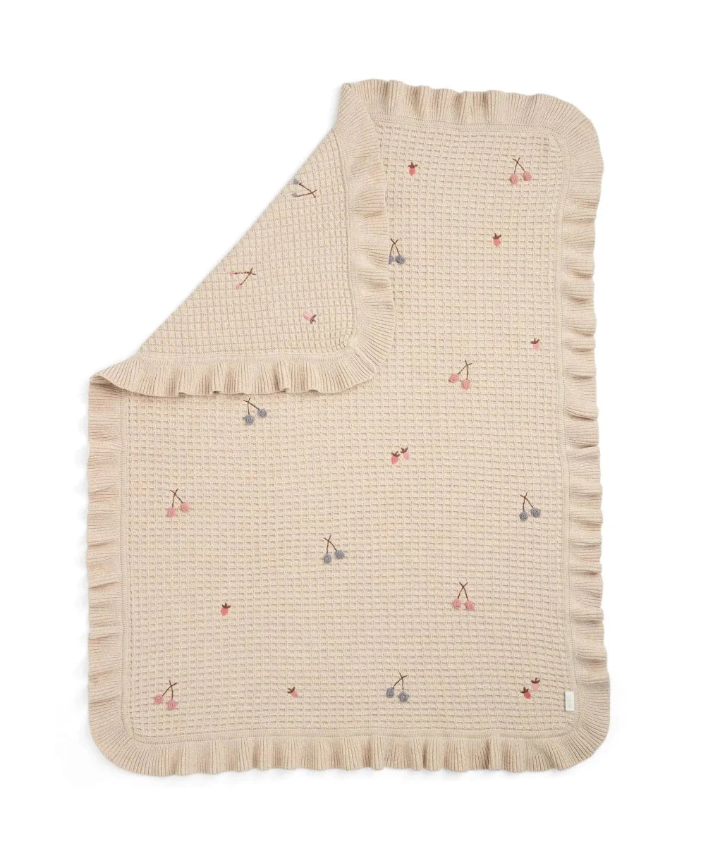 Cream knitted blanket with ruffled edges and small multicolor charm motifs
