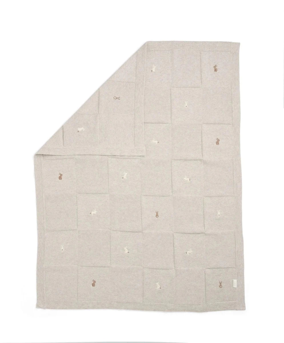 Light grey knitted blanket with small scattered motifs, square fold.