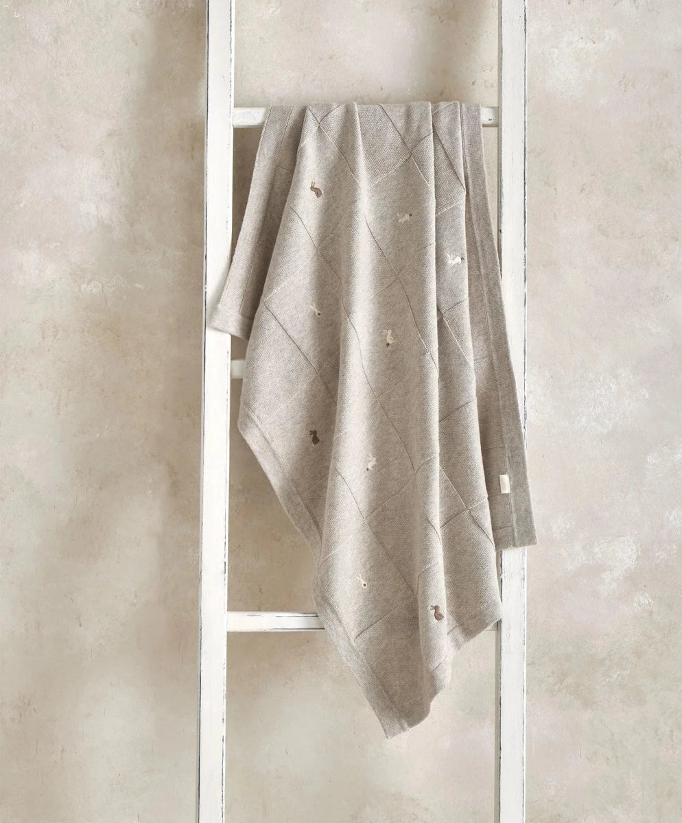 Light grey knitted blanket with scattered motifs, draped over frame.