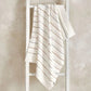 Cream knitted throw blanket with thin neutral stripe lines, folded over