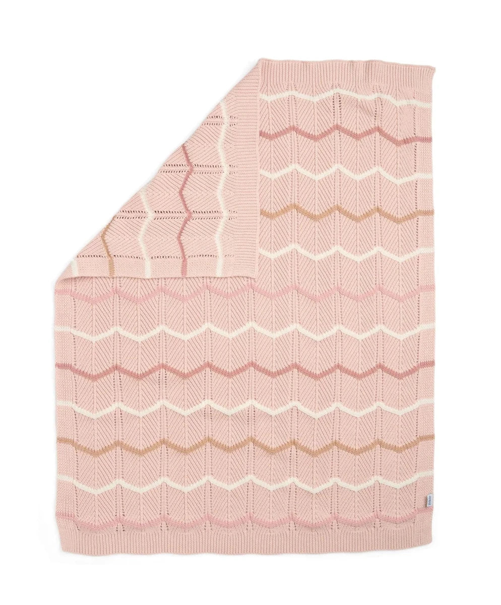 Pink knitted wave blanket with scalloped zigzag pattern, folded edge visible