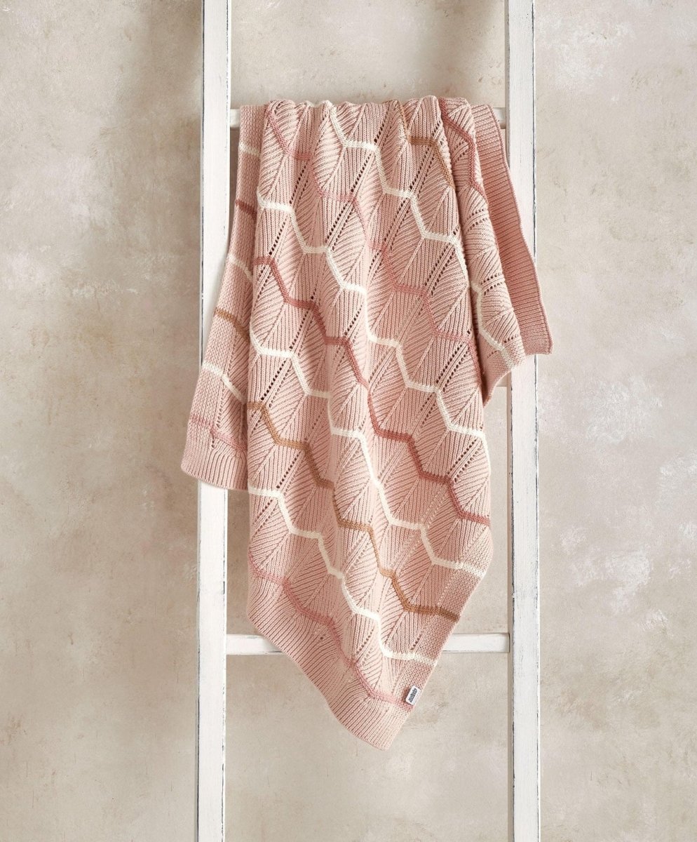 Pink knitted wave blanket draped with white zigzag knit pattern, squared corner