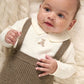 Cream teddy bodysuit with long sleeves and brown knitted dungarees on a baby