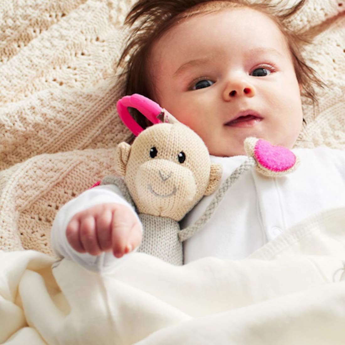 Knitted hanging monkey toy, beige knit body with pink accents, held by baby