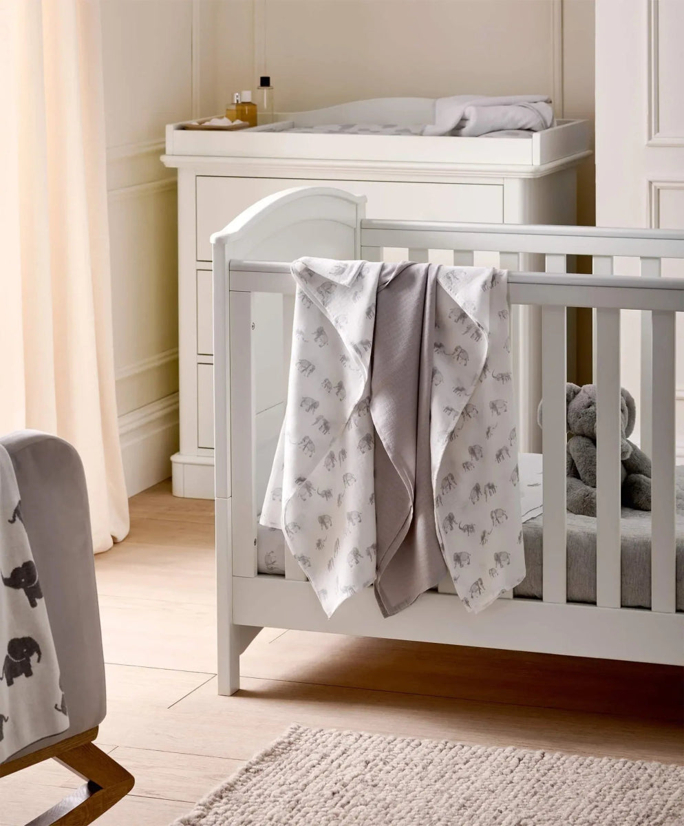 Muslin cloth set hanging from white crib rail, light elephant-print and one plain muslin