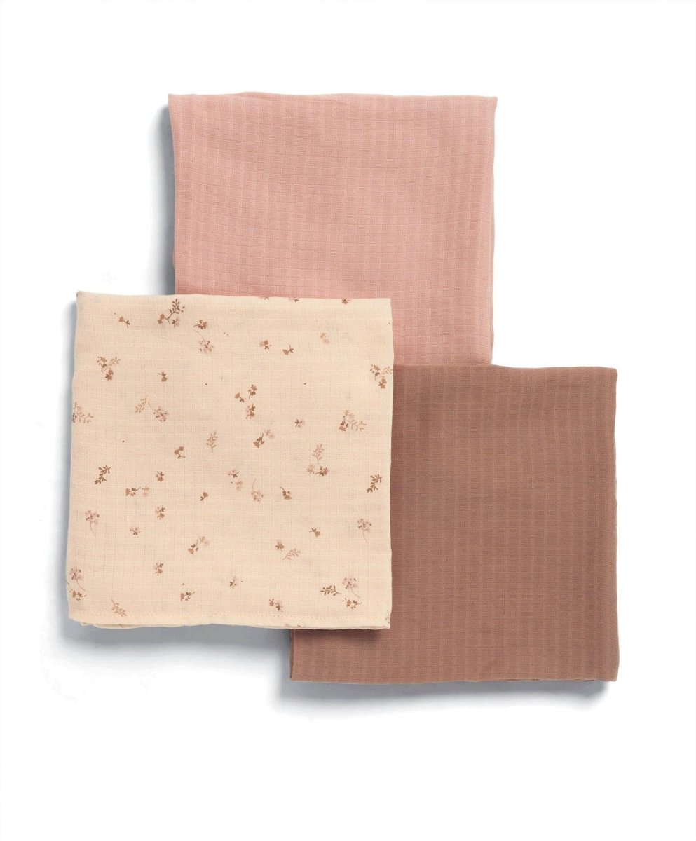 Three muslin cloths folded: cream floral square with two solid pink-toned squares
