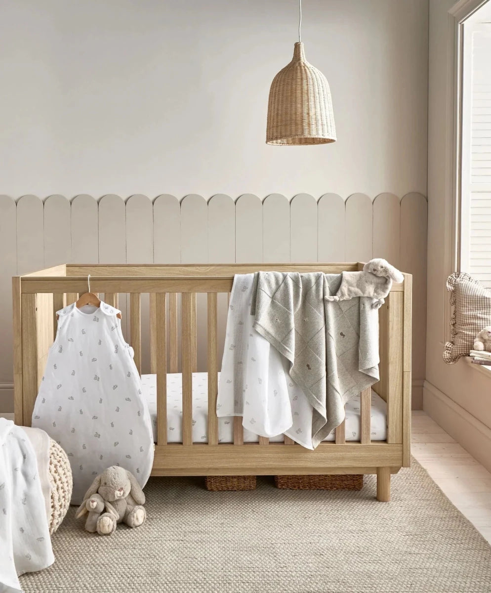 Large muslin squares with bunny print, draped on a crib rail in off-white