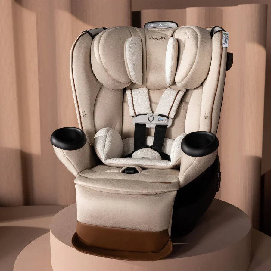 Champagne all-in-one car seat with padded harness and cup holders on dark base, angled.