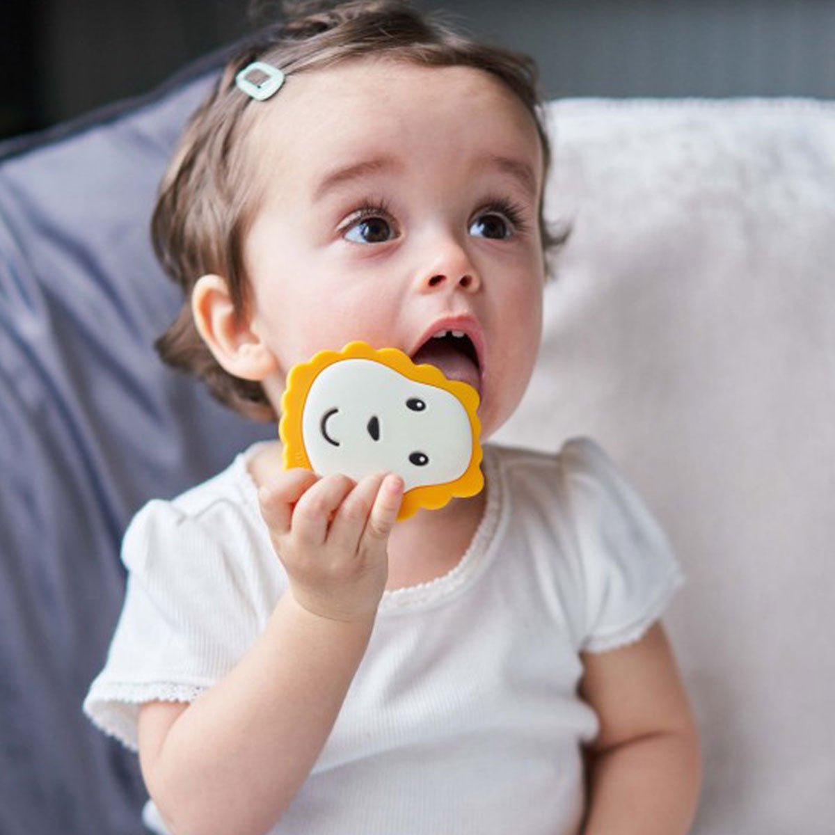 Baby holding a lion-shaped teether with yellow-orange grip and lion face