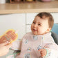 Baby wearing long-sleeved pink bib apron with animal print, mint edging and pocket
