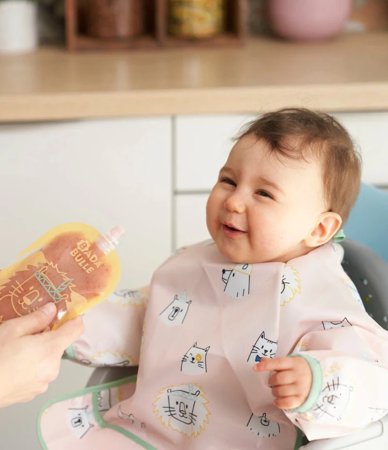 Baby wearing long-sleeved pink bib apron with animal print, mint edging and pocket