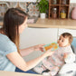 Long-sleeved pink bib apron with animal print, worn on a baby in high chair