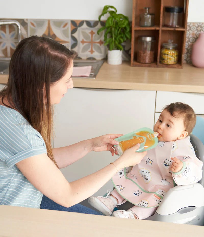 Long-sleeved pink bib apron with animal print, worn on a baby in high chair