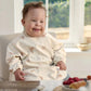 Long-sleeve baby bib in cream with animal print and bib pocket, worn by baby.