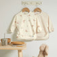 Two long-sleeve baby bibs: cream animal print and pale striped bib set.